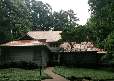 This image shows a single-family house, likely in a wooded suburban setting near Midlothian, Virginia, featuring a prominent and newly installed cedar shake roof.
