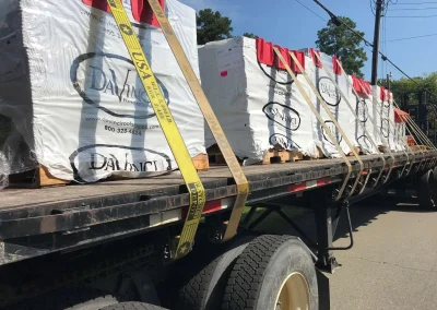 Flatbed truck loaded with multiple shrink-wrapped pallets of slate and cedar roofing materials from DaVinci Roofscapes.