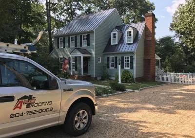 An A Plus Roofing contractor truck parked outside a local home after completing a dark standing seam metal roof replacement.
