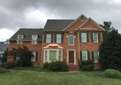 A large brick residential home featuring a new asphalt shingle roof and custom copper metal roofing accents over the bay window, installed by local roofers in Short Pump, VA.